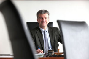 Werner Steinecker in seinem Büro mit schwarzen Stühlen im Vordergrund
