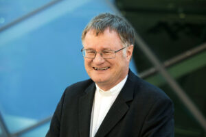 Bischof Manfred Scheuer draußen vor einer Fensterfront