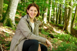 LR Michaela Langer-Weninger im Wald auf einem Baustamm sitzend