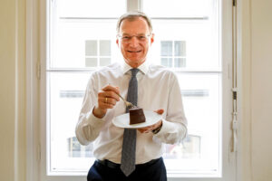 LH Thomas Stelzer beim Kuchen essen vor einem Fenster
